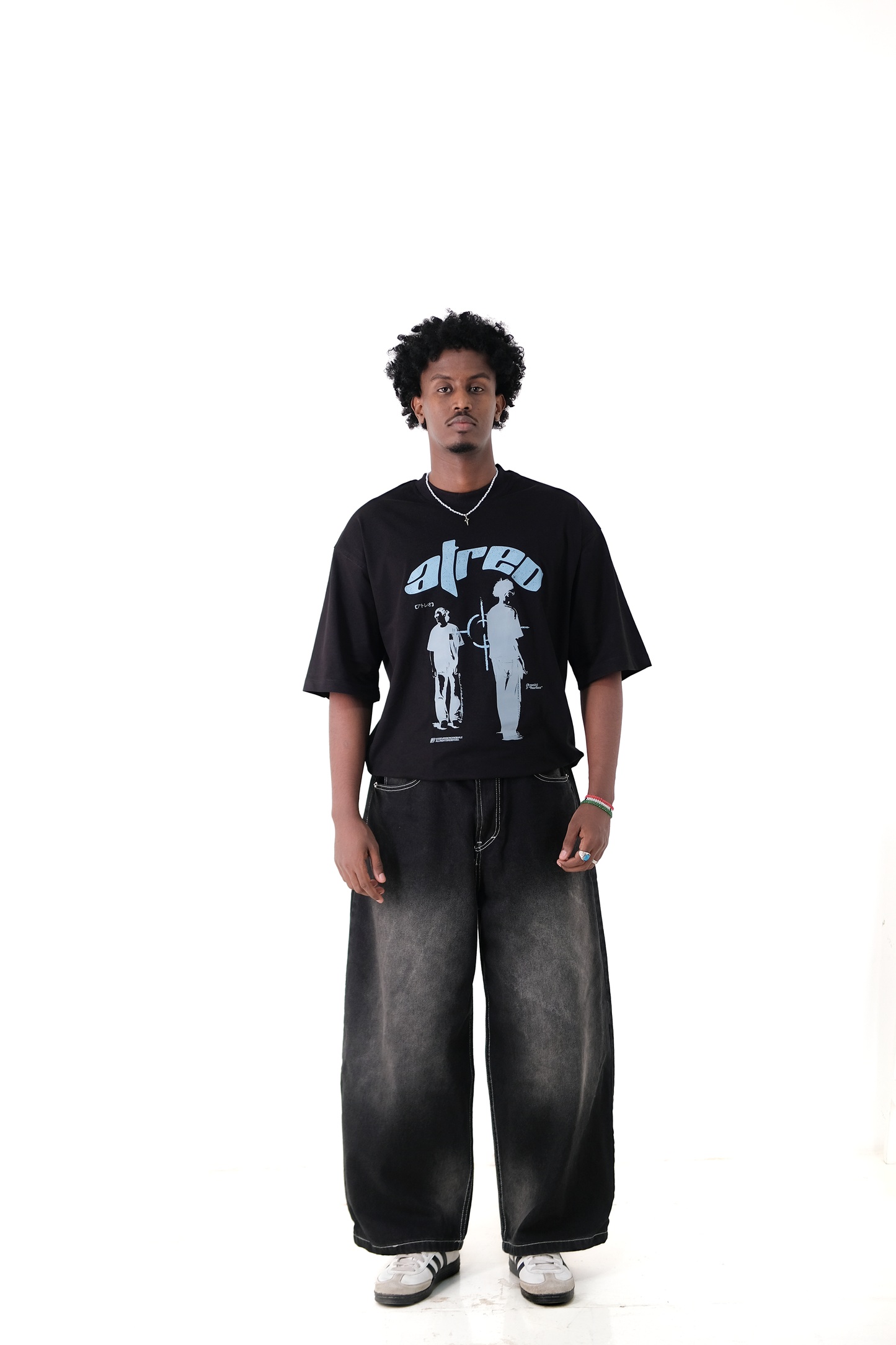 Front view of a male model wearing Version Originale’s “Atreo” tee in graphite black with blue graphic print, paired with Version Originale’s baggy faded black denim Tony Hawk jeans