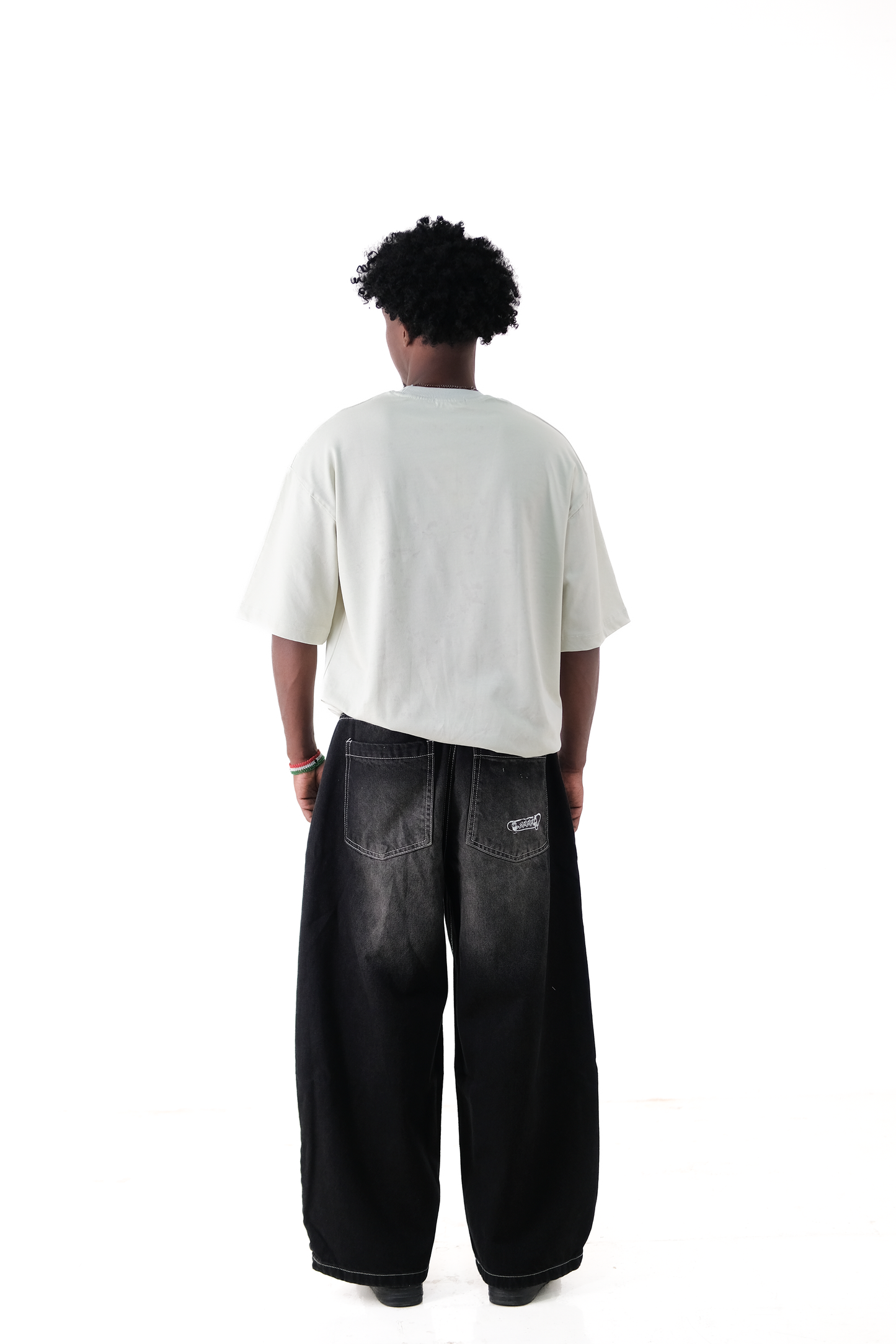 Back view of a male model wearing Version Originale’s oversized lime green tee paired with Version Originale’s baggy faded black Tony Hawk jeans, featuring subtle back pocket print paying tribute to Tony Hawk’s iconic 900 spin at the 1999 X Games
