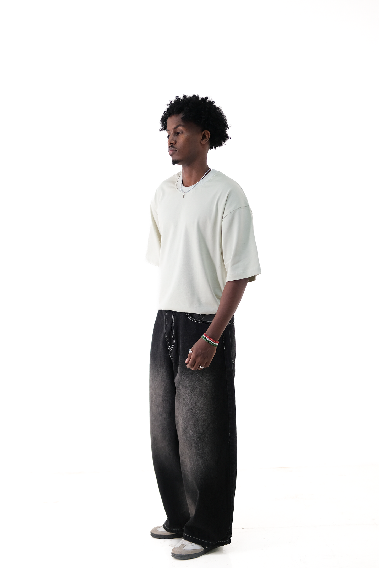 Side view of a male model wearing Version Originale’s oversized lime green tee paired with Version Originale’s baggy faded black denim Tony Hawk jeans