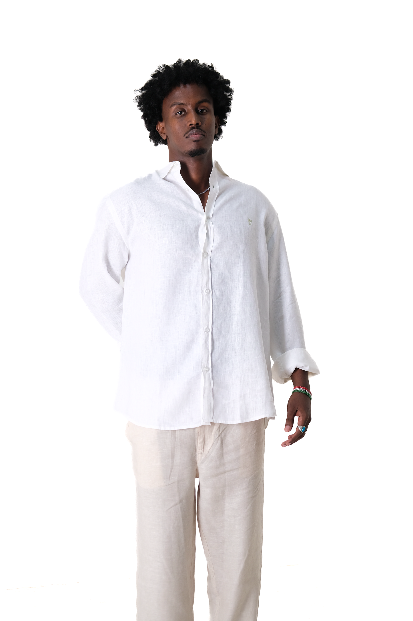 Male model in Version Originale's classic white linen shirt with green palm tree chest embroidery, paired with Version Originale's beige linen pants — captured from a front-facing relaxed pose