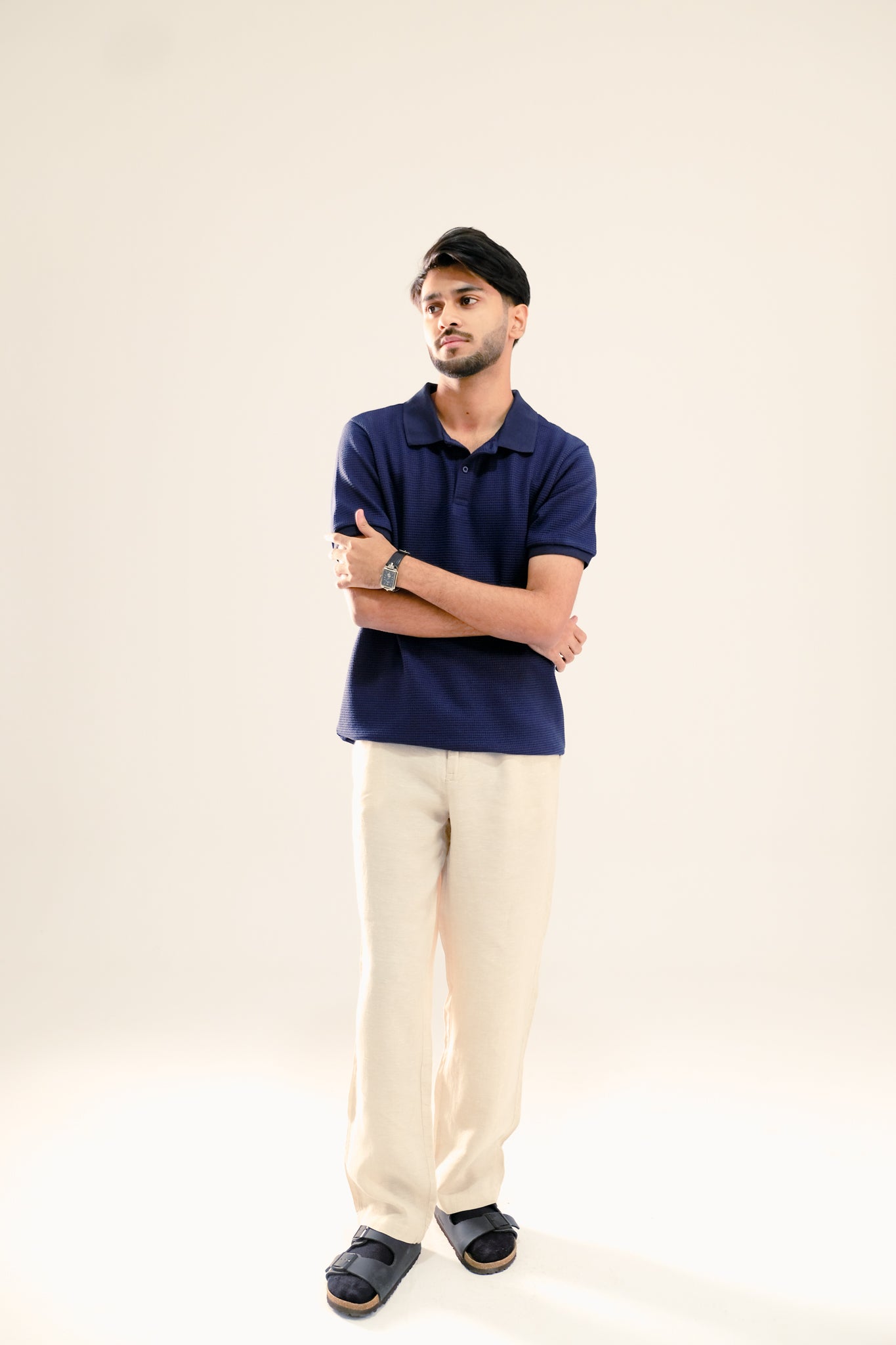 Man wearing a blue polo shirt and beige pants against a plain background