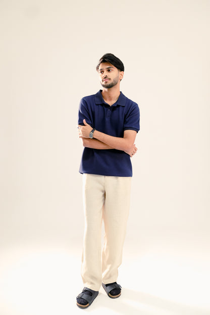 Man wearing a blue polo shirt and beige pants against a plain background
