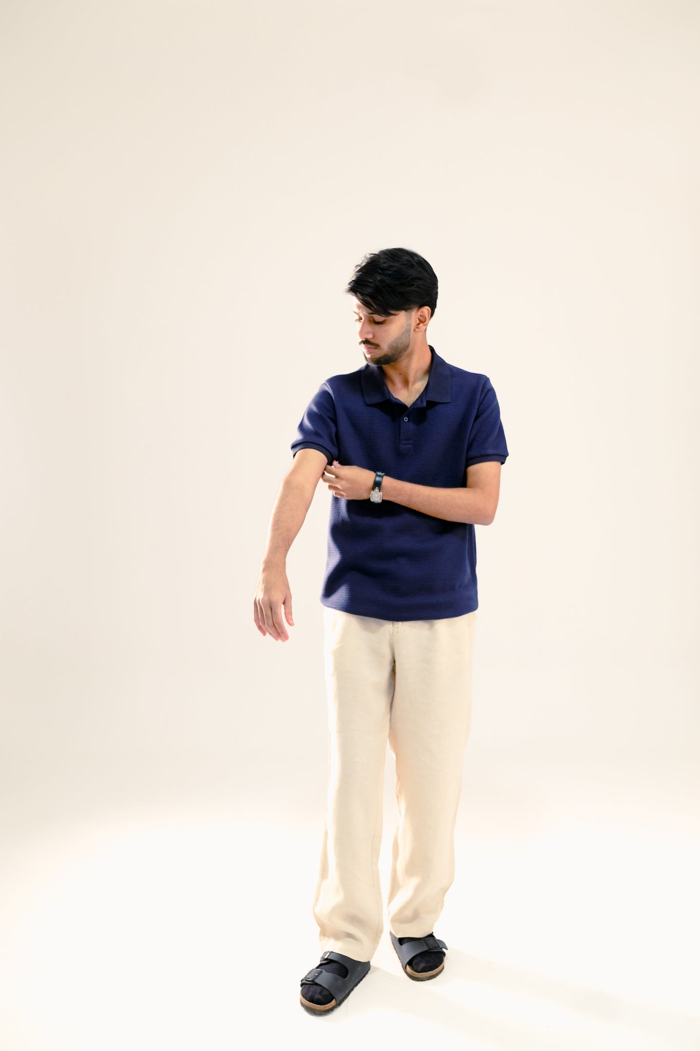 Man wearing a navy blue polo shirt and beige pants against a light background