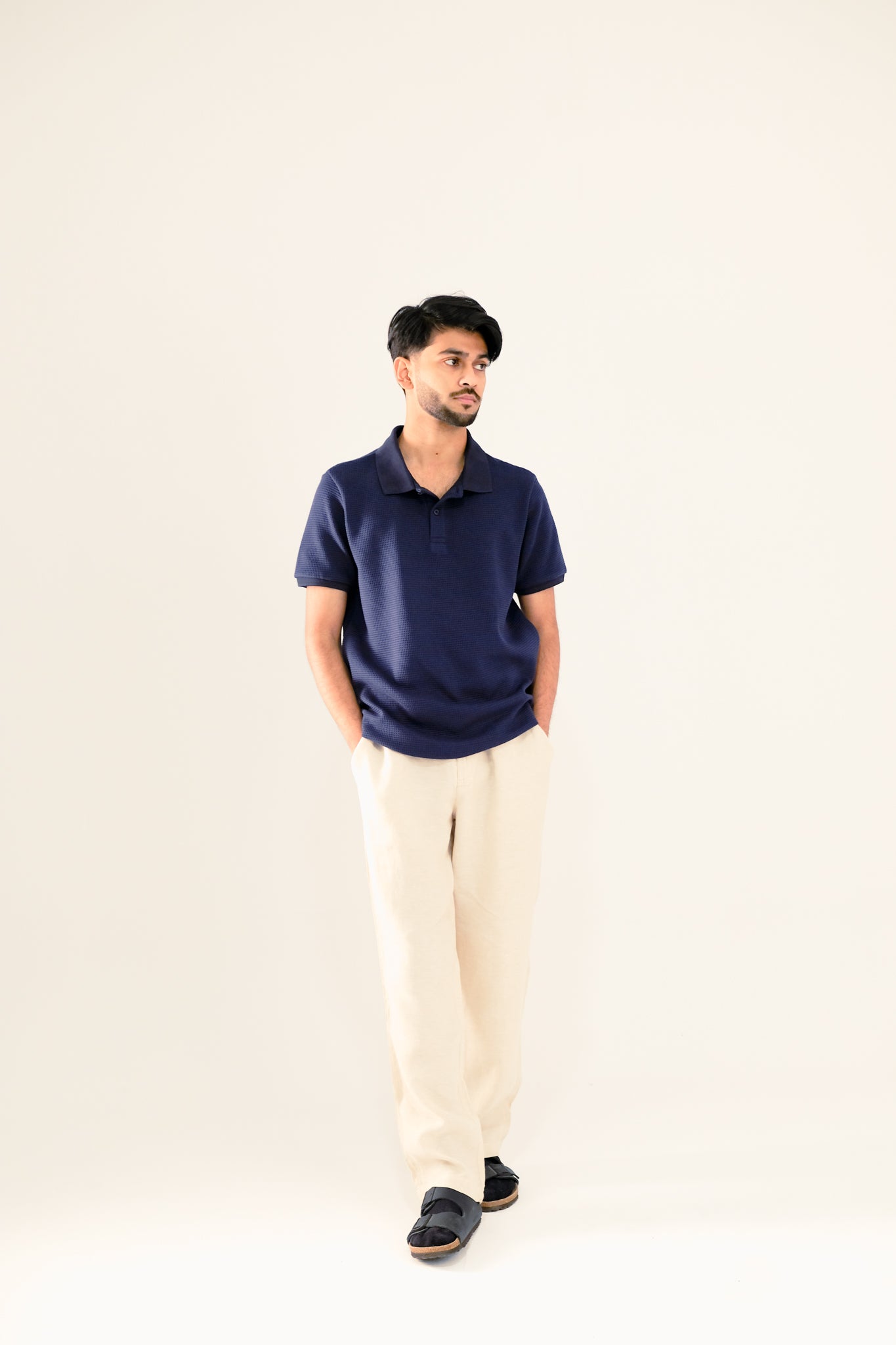 Man wearing a navy polo shirt and beige pants against a white background