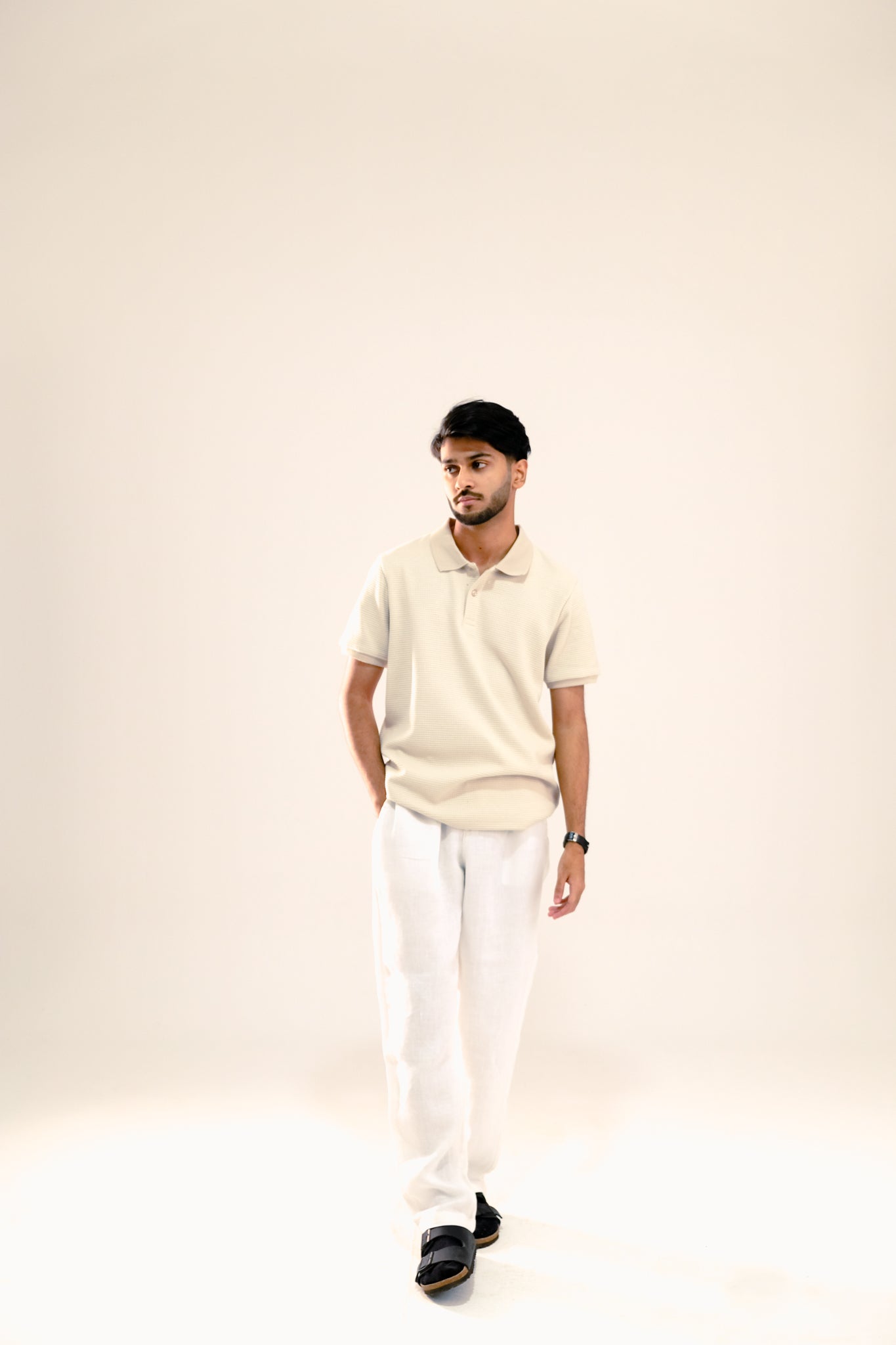 Man wearing a beige polo shirt and white pants on a plain background