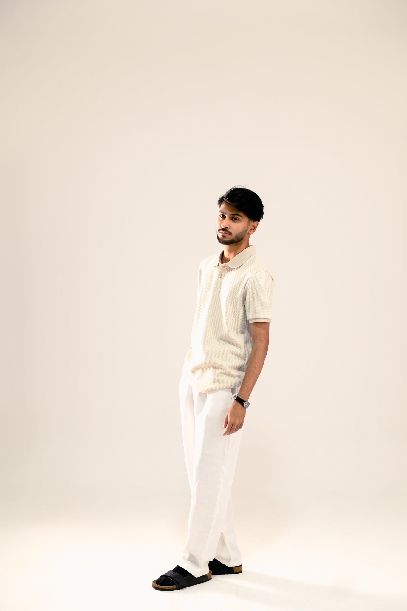 Man wearing a white polo shirt and pants against a plain background