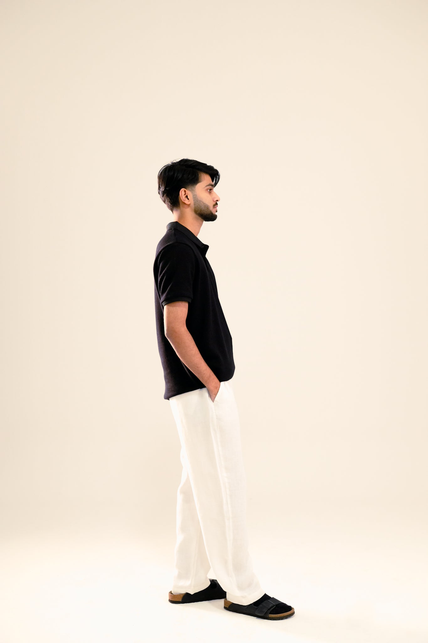 Man wearing a black polo shirt and white pants on a beige background