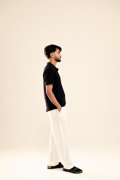 Man wearing a black polo shirt and white pants on a beige background