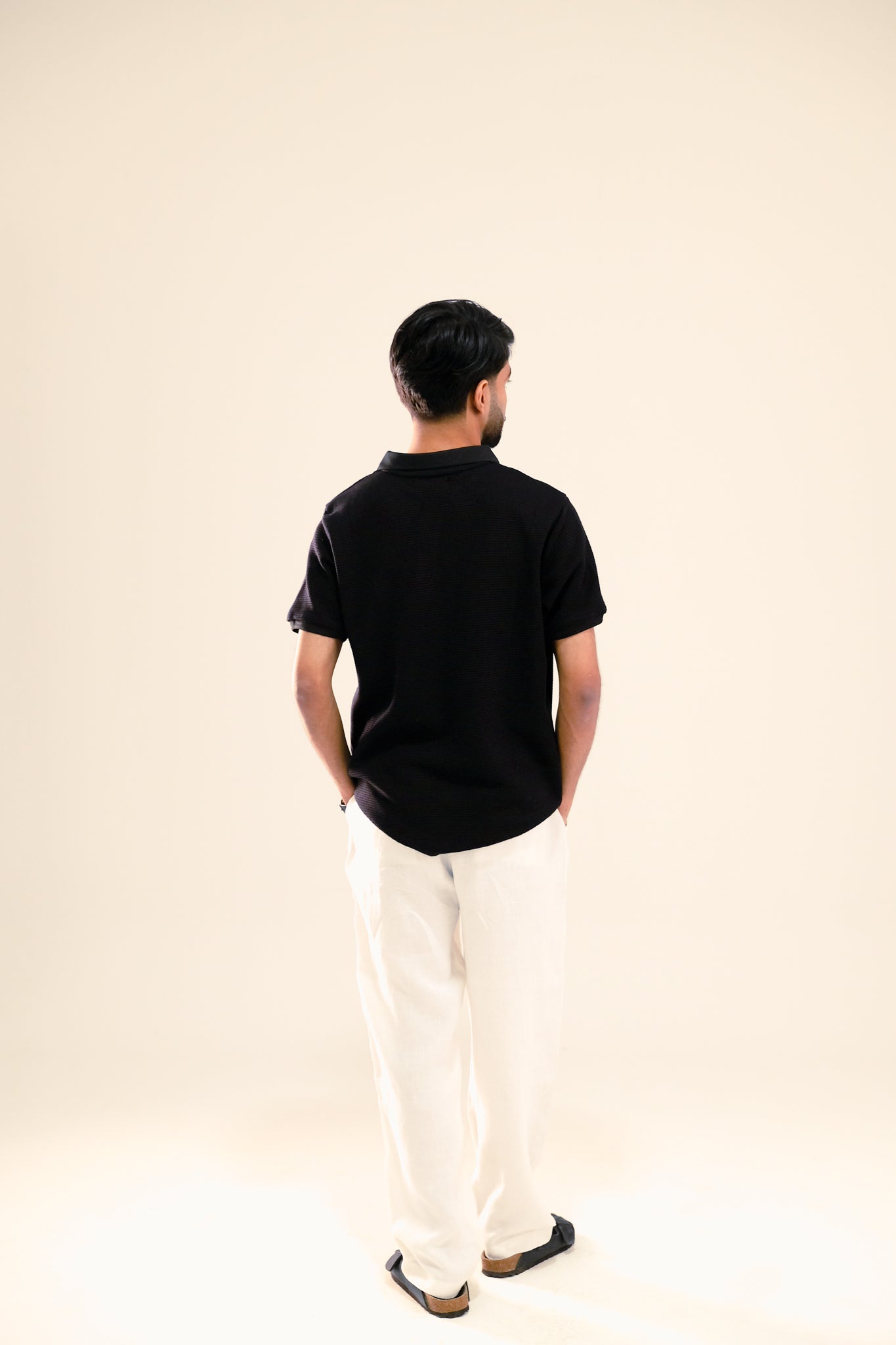 Man wearing a black polo shirt and white pants on a beige background