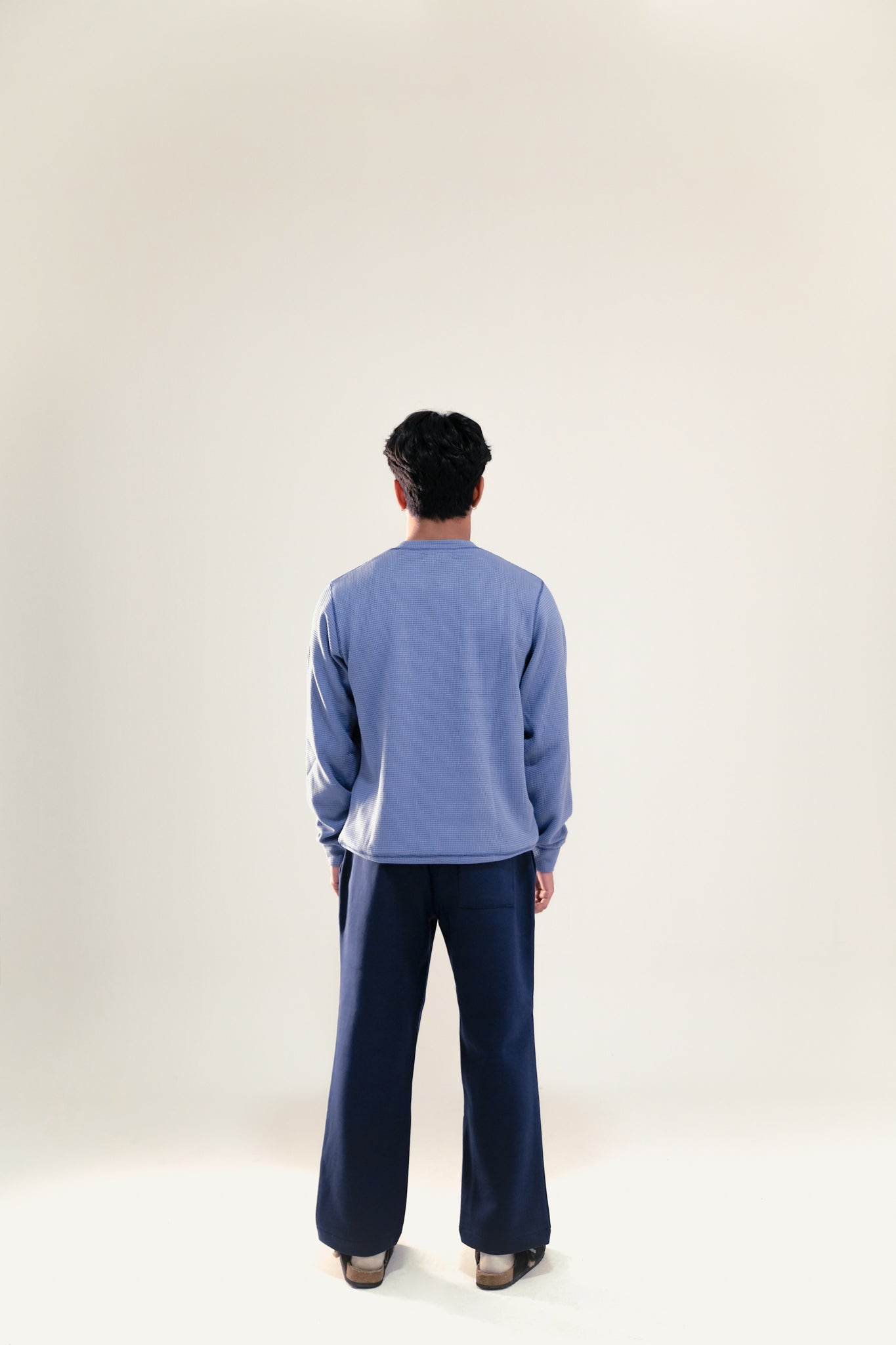 Man facing backwards wearing blue waffle knit sweatshirt and navy blue sweatpants against a white background