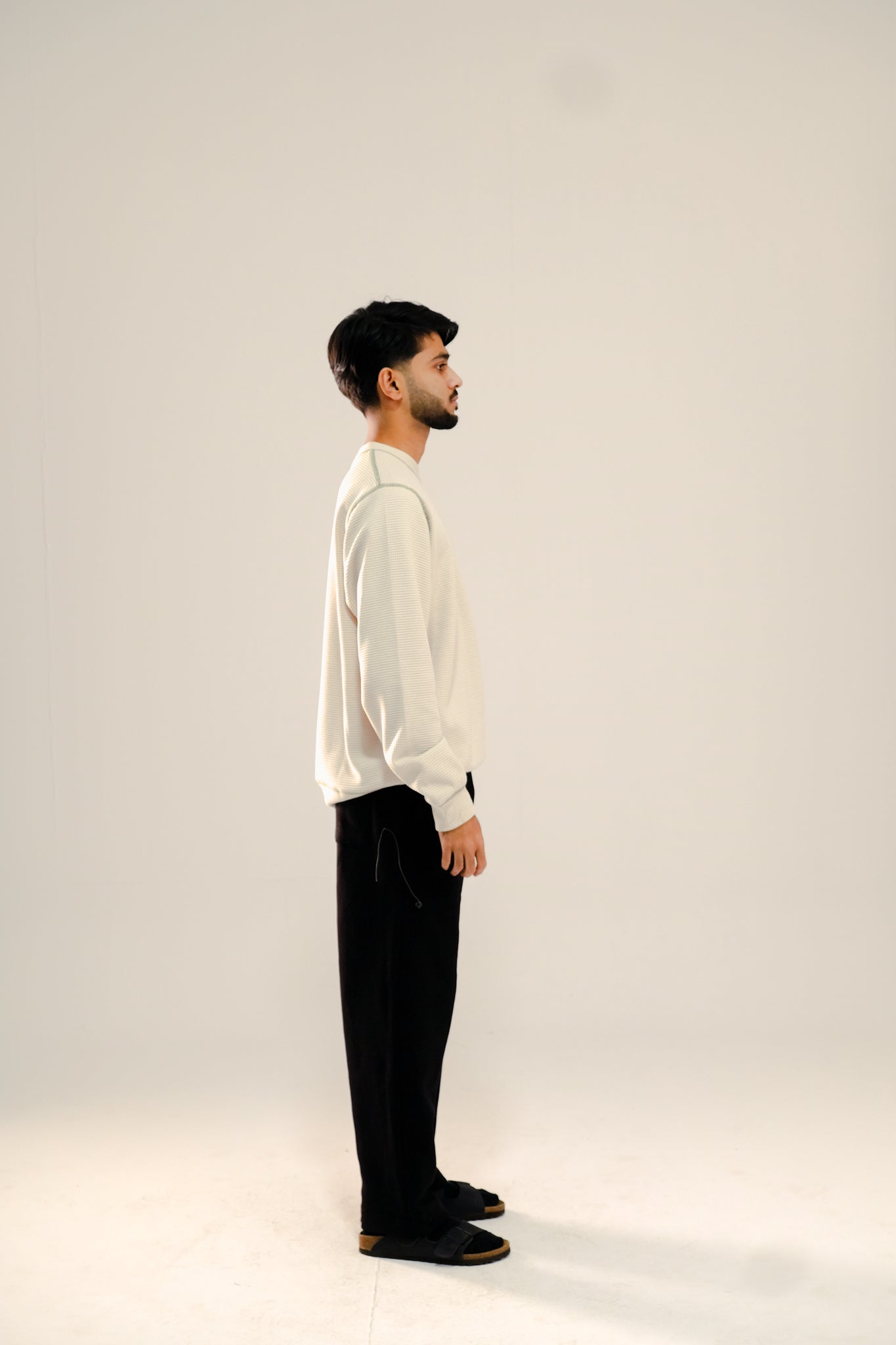 Man wearing a beige waffle knit sweatshirt and black sweatpants standing against a beige background