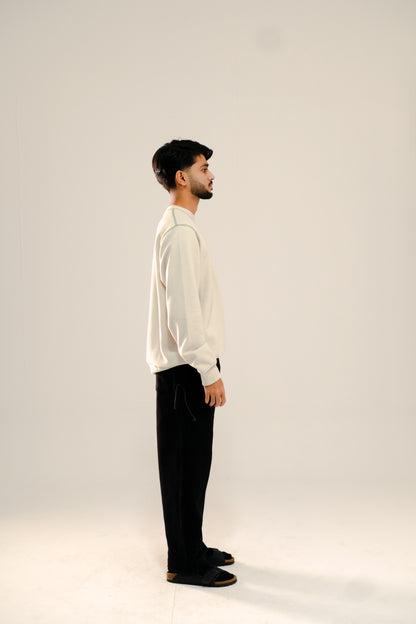 Man wearing a beige waffle knit sweatshirt and black sweatpants standing against a beige background