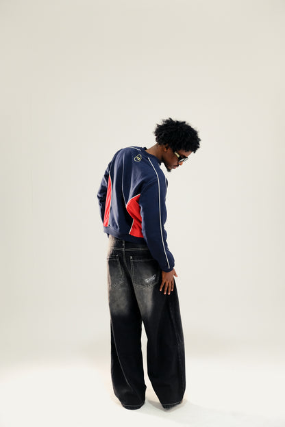 Model wearing navy blue and red vintage sweatshirt with black washed baggy jeans and sunglasses against a white background