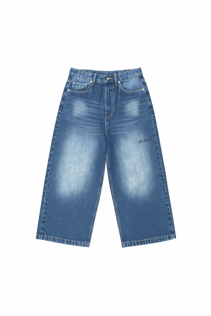 Flat lay of Version Originale’s faded denim blue jeans featuring a relaxed wide-leg cut, subtle whiskering, and a dark “La Mémoire” print