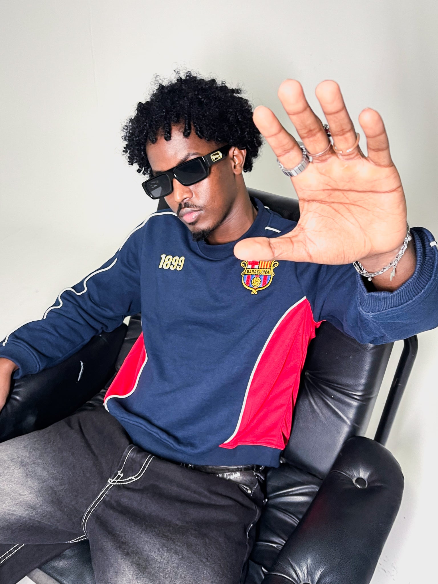 Model sitting on chair wearing navy blue and red vintage Barcelona sweatshirt against a white background