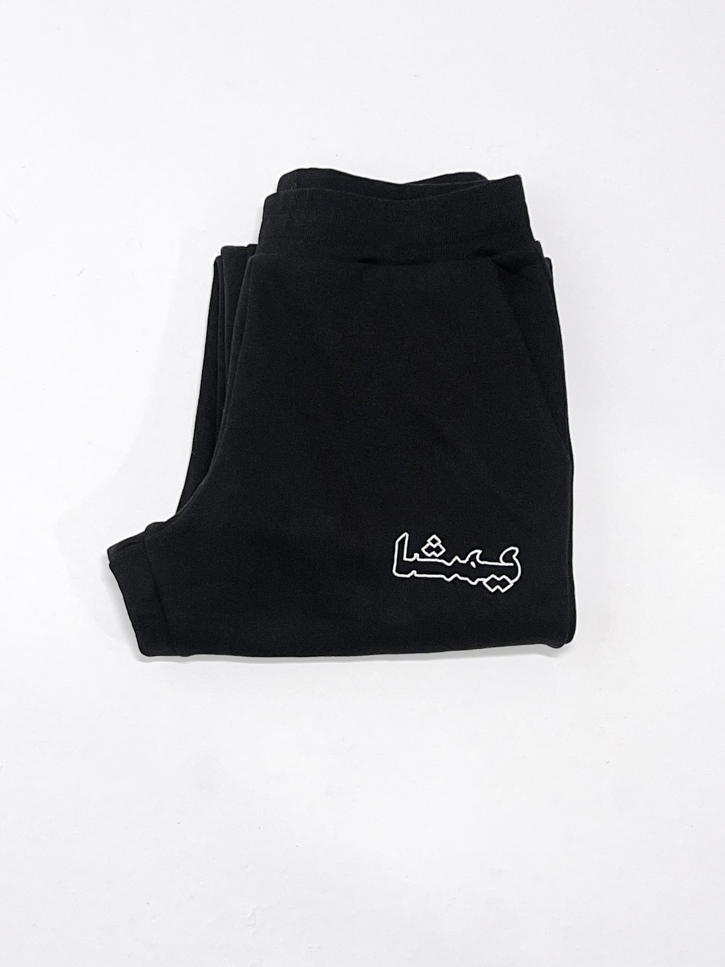 Folded black sweatpants with an arabic print against a white background