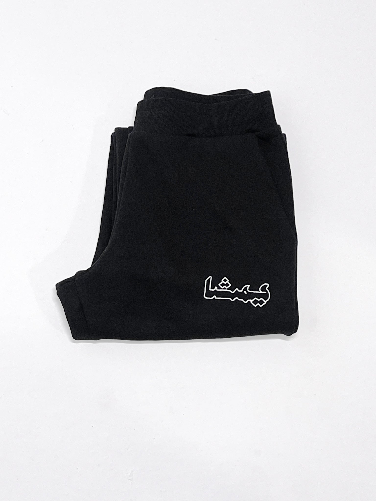 Folded black sweatpants with an arabic print against a white background
