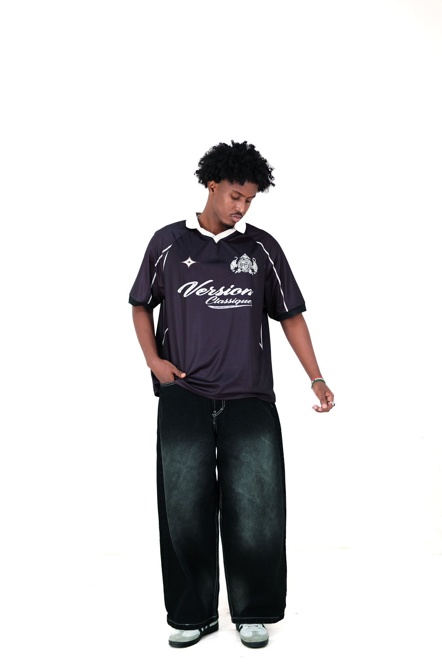 Male model wearing Version Originale’s black athletic jersey with “Version Classique” text and crest on the front, paired with Version Originale's wide-leg black faded jeans and sneakers, standing against a white background
