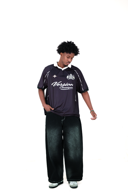 Male model wearing Version Originale’s black athletic jersey with “Version Classique” text and crest on the front, paired with Version Originale's wide-leg black faded jeans and sneakers, standing against a white background