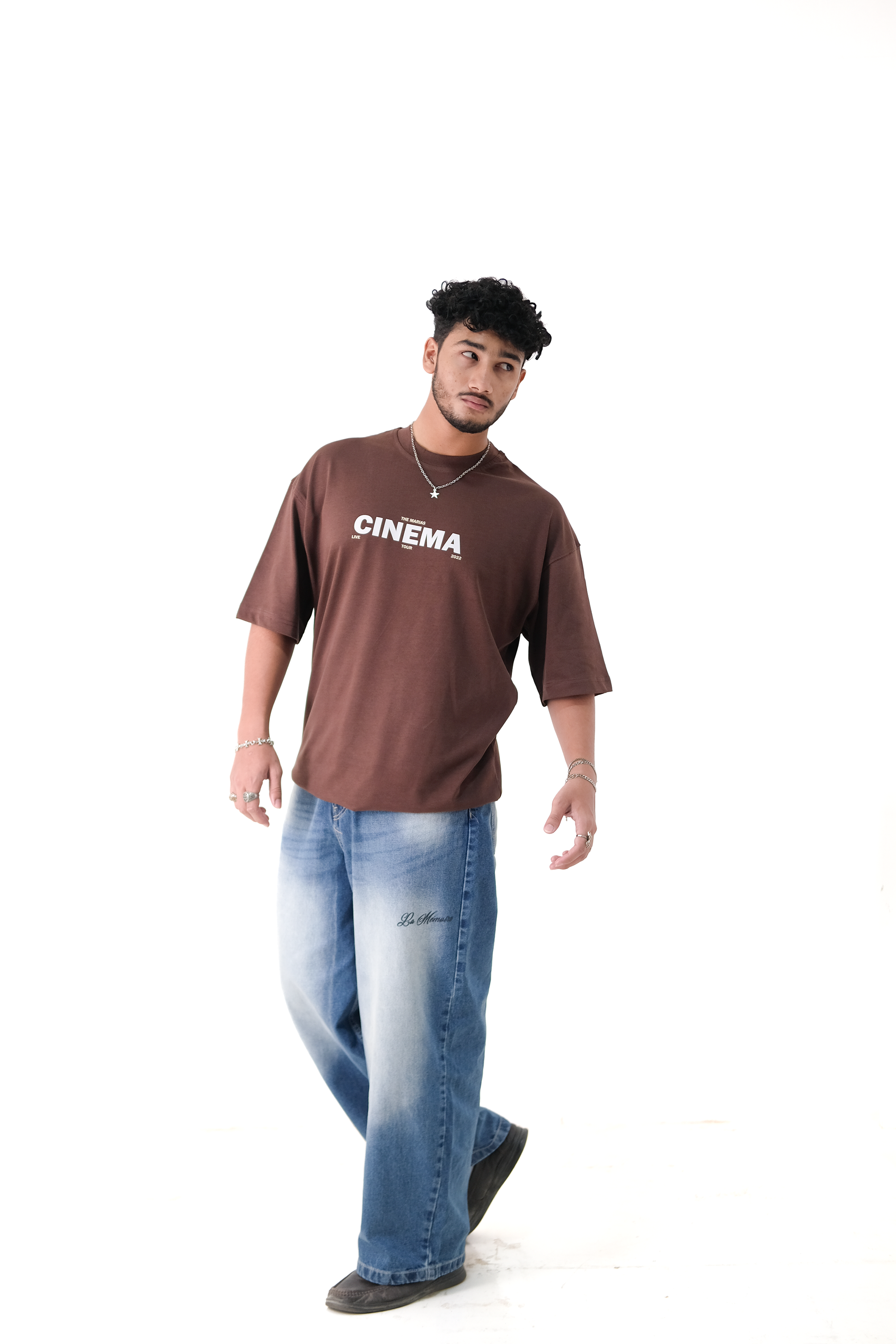 Male model showcasing Version Originale streetwear style, wearing oversized cocoa brown “Cinema” t-shirt paired with Version Originale’s faded denim blue jeans featuring dark “La Mémoire” print
