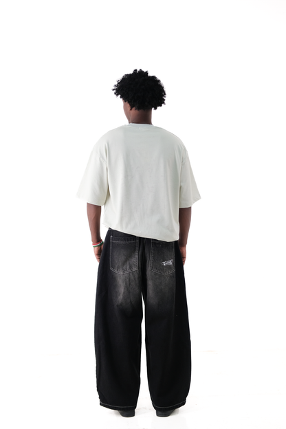 Back view of a male model wearing Version Originale’s oversized lime green tee paired with Version Originale’s baggy faded black Tony Hawk jeans, featuring subtle back pocket print paying tribute to Tony Hawk’s iconic 900 spin at the 1999 X Games